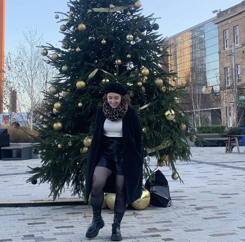 Sophie is pictured smiling on University of Leicester campus, in front of a gold-decorated Christmas tree. 